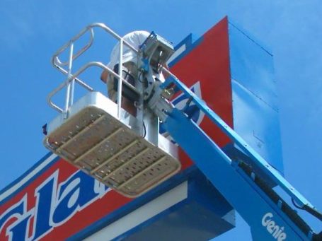 Leo using a lift to maintain a large outdoor sign against a clear blue sky.