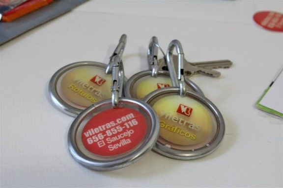 Three keyrings with round tags, one red and two with yellow backgrounds, displaying various text.