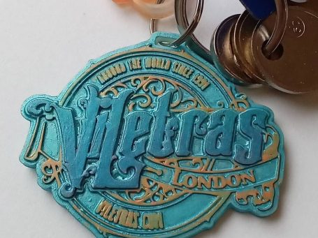 A vibrant turquoise and gold keychain featuring the word "Viletras" and "London."